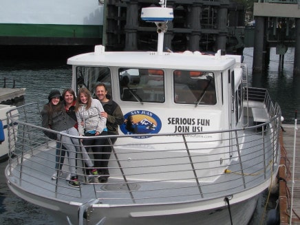 Four people standing on the deck of a small whale watching boat