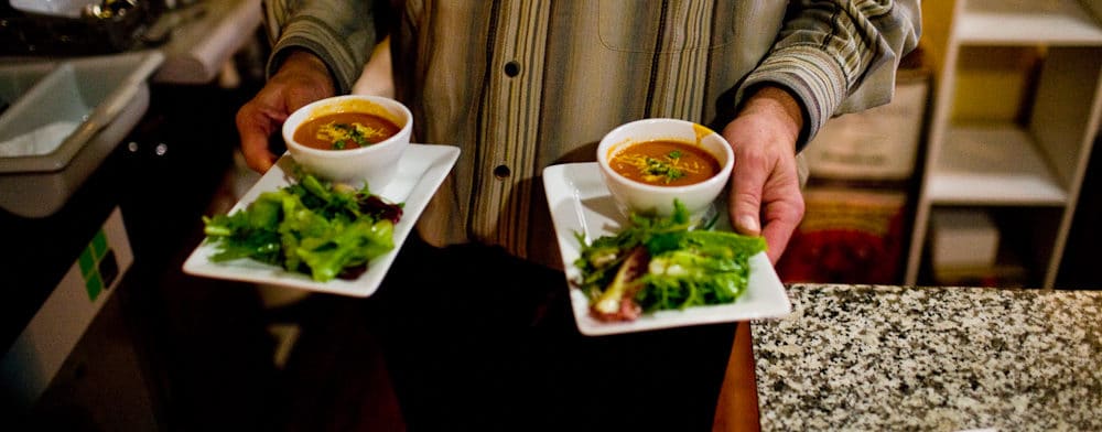 hands holding two plates of salad and soup