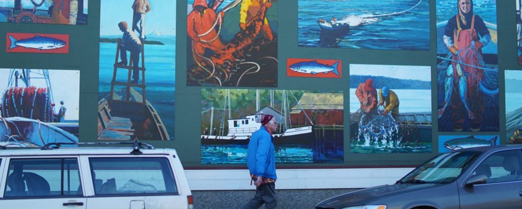 man in a blue jacket walking down a street in front of a large mural