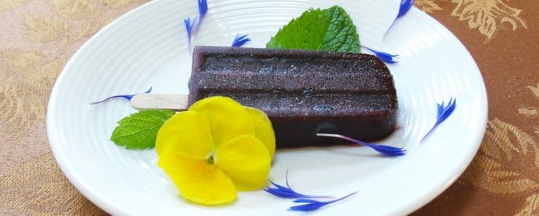 purple popsicle on a plate with a yellow pansey garnish
