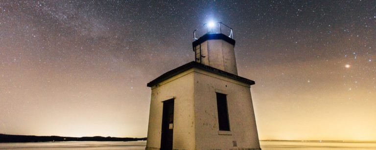 small lighthouse lit up at night under the stars