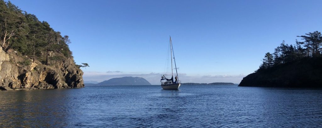 sailboat cruising past a ricky shoreline