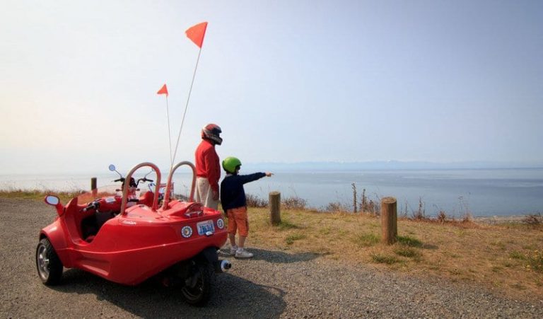 man and child wearing helmets near a red scooter looking out over the water