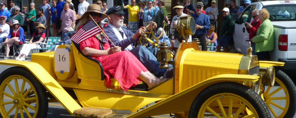couple driving an antique yellow car in a parade