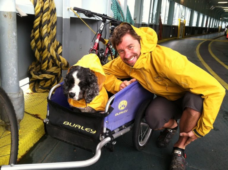 man crouched down next to his dog riding in a wagon