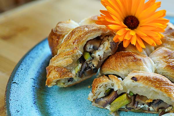 Pastry stuffed with mushrooms, asparagus and cheese on a blue plate with orange flower garnish