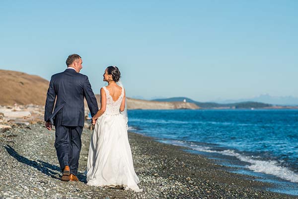 Bride and groom holding hands walking along a rocky beach