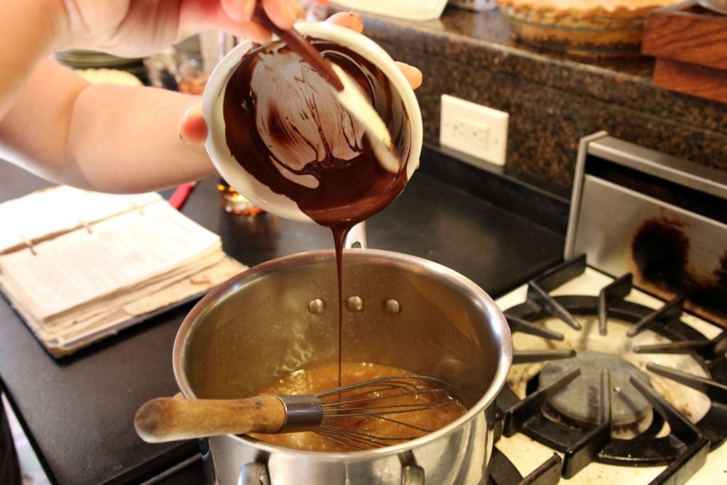 bowl of melted chocolate being scraped into a pot on a stove