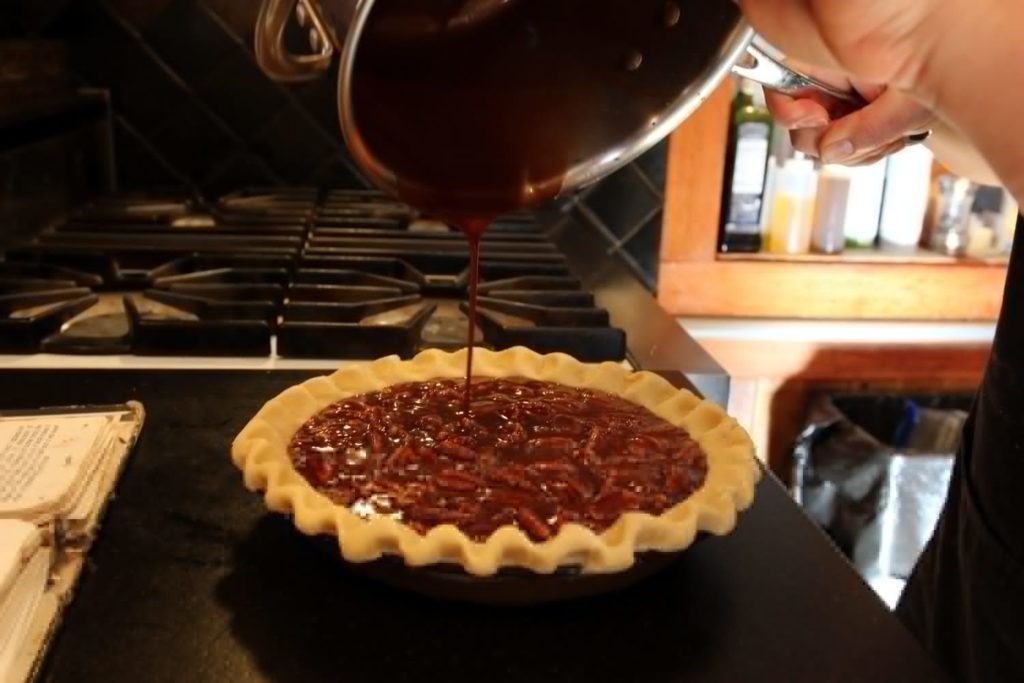Unbaked shell being filled with pecan pie filling
