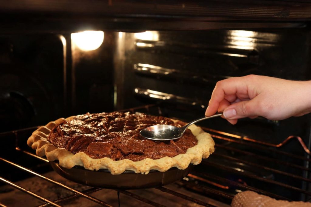 Pecan pie on an oven rack being tapped with the back of a spoon