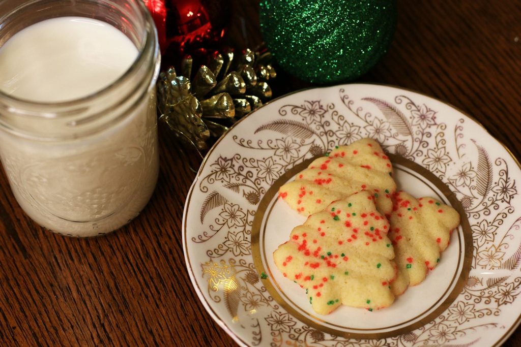 Three decorated Butter Spritz Cookies with a glass of milk