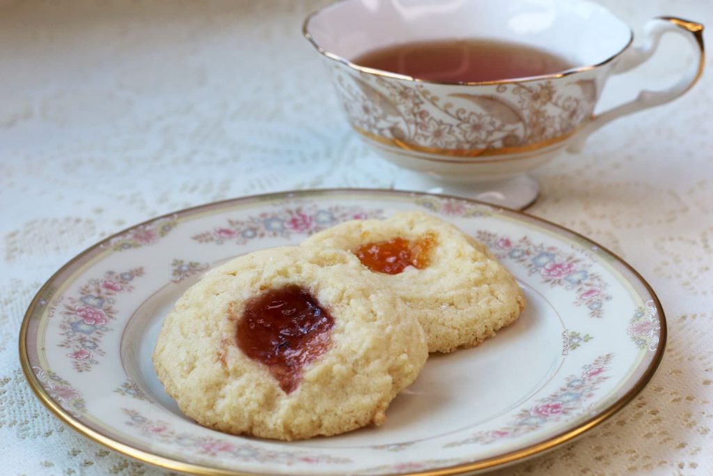 Two Thumbprint Cookies on a china plate with a cup of tea
