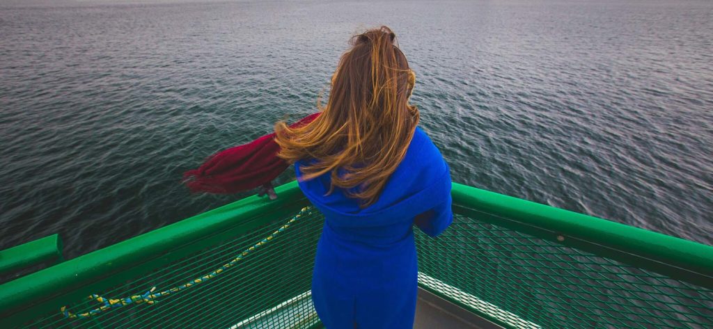 Woman wearing a blue dress looking out across the water from the ferry deck