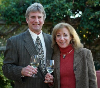 Couple in formal dress holding wine glasses and smiling at the camera