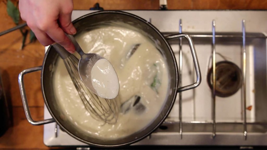 Spoon full of béchamel sauce over a pot on a small stove