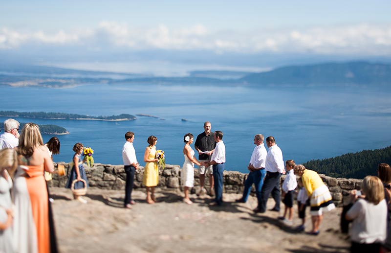 Bride and groom standing with guests for a ceremony at a lookout with views of the water and neighboring islands