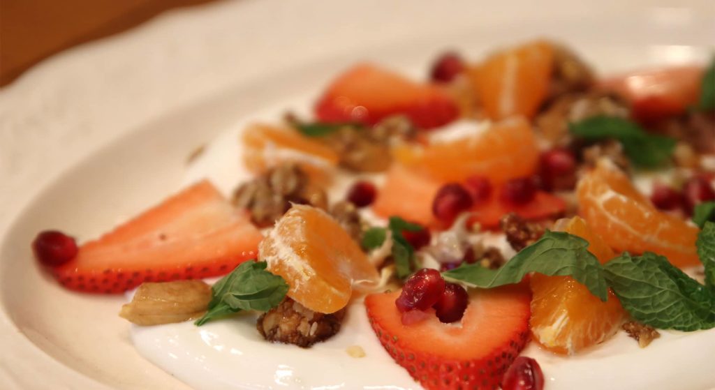 yogurt plate with slices or orange, strawberries, and mint on top