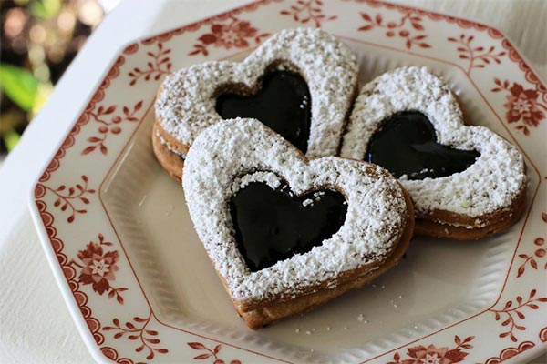 three heart-shaped powdered sugar covered cookies on a red and white china plate