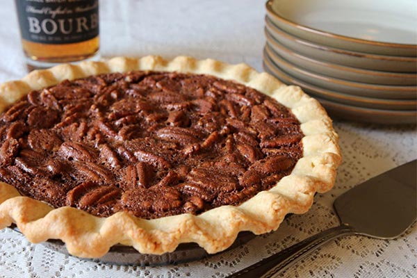 pecan pie with a stack of plates and bottle of bourbon behind