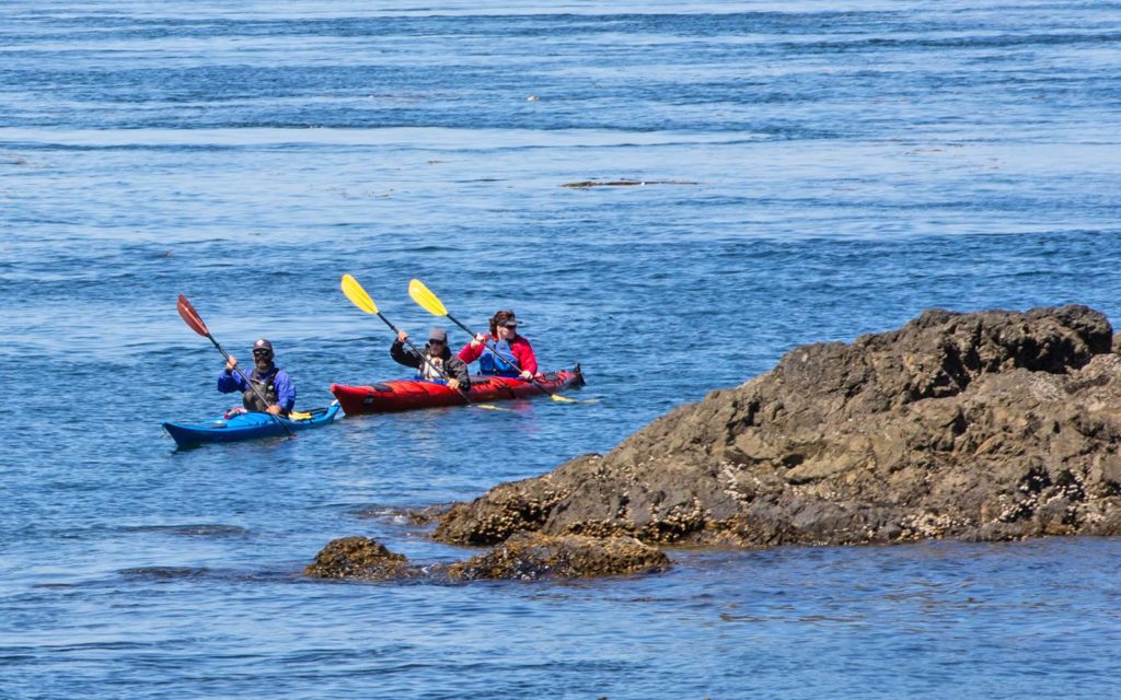 three people kayaking near a rocky outcrop