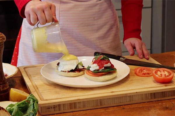 Chef pouring hollandaise sauce over Eggs Benedict