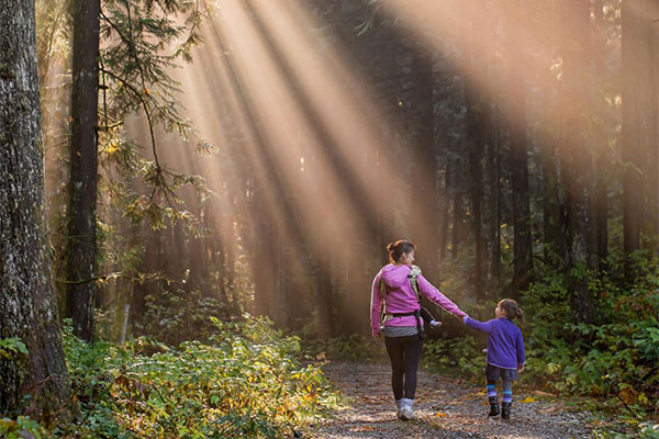 Mother and daughter hiking on a wooded path with sunlight streaming through