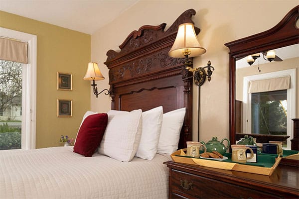 dark wood bed frame with cream quilt, sconces, and red velvet pillow