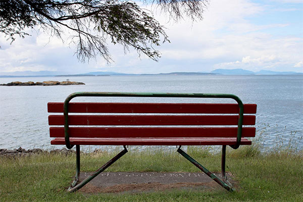 empty red park bench facing out towards the water